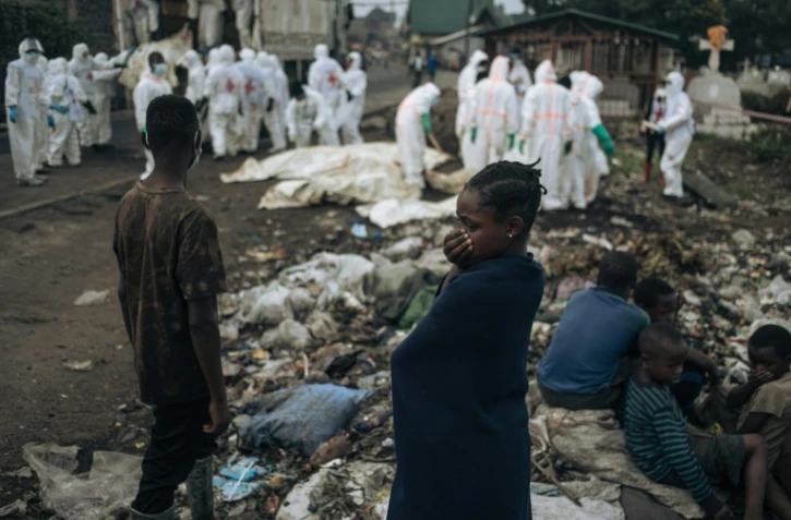 De jeunes habitants regardent des membres de la Croix-Rouge congolaise et de la Protection civile enterrer des dizaines de corps, le 3 février 2025 dans un cimetière de Goma en RDC