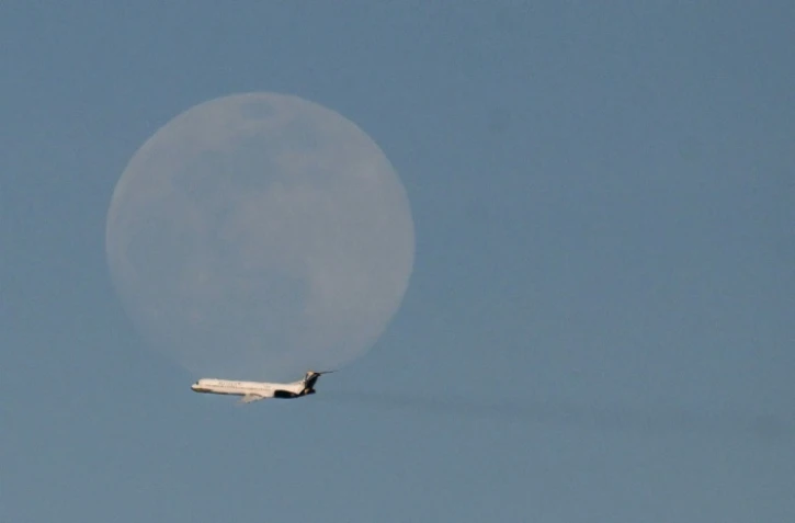 Un avion de la compagnie vénézuélienne Rutaca passe devant la lune, vu depuis l'aéroport international Simon Bolivar à Maiquetia, Venezuela, le 3 décembre 2025