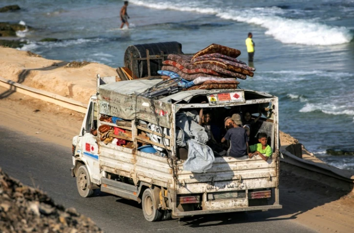 Des déplacés palestiniens fuyant le nord de la bande de Gza en direction du sud du terrtoire roulent à bord d'un camion chargé d'effets personnels sur la route côtière du camp de Nousseirat (centre), le 30 août 2025