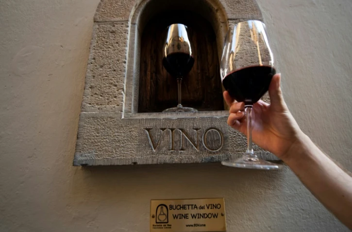 Une personne tient un verre de vin à côté d'une "fênêtre à vin" dans une rue de Florence, le 12 août 2020 en Italie