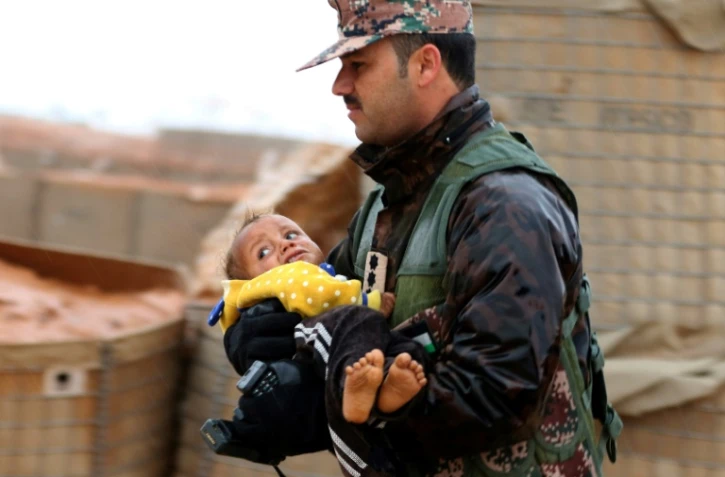 Un membre des forces armées jordaniennes transporte un enfant dans une zone tampon à la frontière entre la Syrie et la Jordanie, le 1er mars 2017