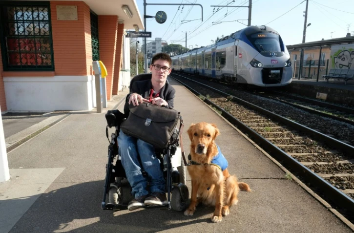 Kevin Fermine, 25 ans, atteint du "syndrome de Little" (dégénérescence des neurones) et en fauteuil roulant depuis son plus jeune âge, pose avec son chien Djembe le 16 mars 2017 à la gare Saint-Agne de Toulouse