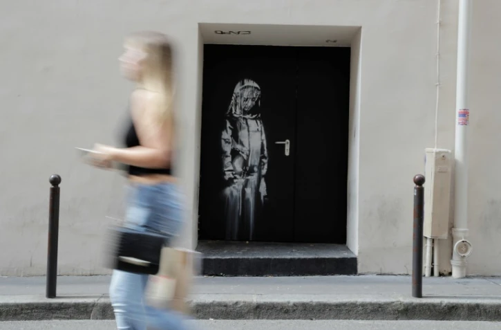 Une femme passe devant le pochoir de l'artiste Bansky le 25 juin 2018, dans une rue près de la salle de concert du Bataclan