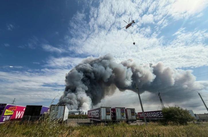 Un hélicoptère bombardier d'eau s'apprête à faire un largage au-dessus d'un incendie dans un centre logistique du géant russe de l'e-commerce Wildberries, le 16 août 2026 à Podolsk, près de Moscou

