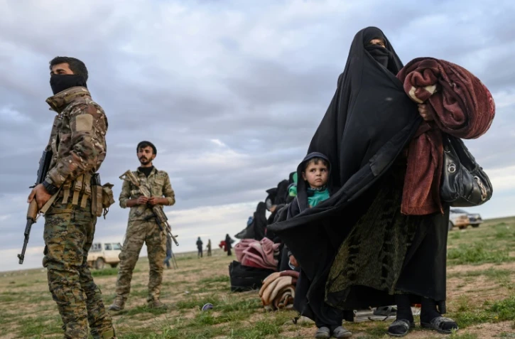 Une femme et son enfant passent devant des membres des Forces démocratiques syriennes, après avoir fui le dernier réduit du groupe Etat islamique à Baghouz, en Syrie, le 28 février 2019 