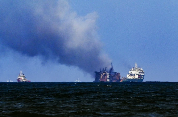 Un bateau de la société néerlandaise Smit remorque le porte-conteneurs MV X-Press Pearl (c), ravagé par un incendie depuis douze jours, pour l'éloigner des côtes de Colombo, le 2 juin 2021 au Sri Lanka
