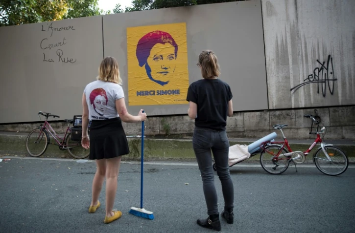 Les artistes de rue Eleanor et Juliette du collectif  "Merci Simone" devant un poster du portrait de Simone Veil qu'elles viennent de poser à Paris, le 28 juin 25018