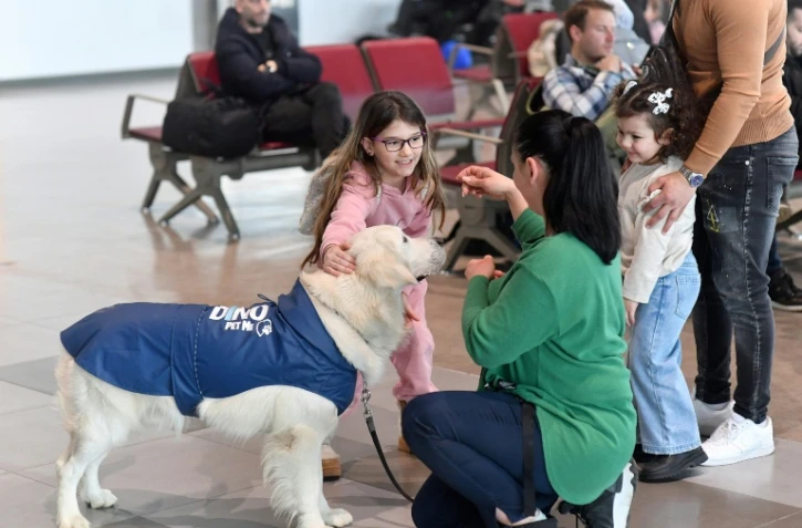 Des enfants s'approchent de Dino, un golden retriever conduit par sa dresseuse Vesna Kiskovska (d) à l'aéroport international de Skopje, le 29 janvier 2025 en Macédoine du Nord