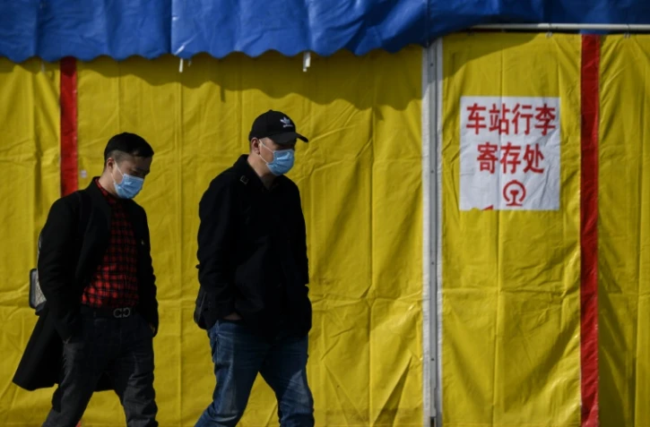 Deux hommes portant des masques de protection contre le coronavirus marchent dans une rue de Jiujiang, le 19 mars 2020 en Chine