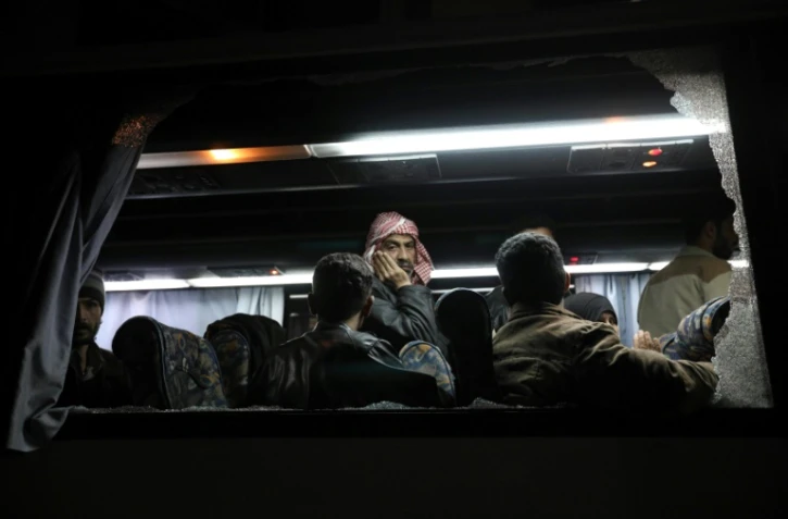 Des rebelles et civils syriens évacués de leur ancien fief dans la Ghouta orientale après des semaines de bombardements du régime, dans un bus arrivant à Qalaat al-Madiq, le 31 mars 2018, étape avant leur destination finale dans la province d'Idleb au nord-ouest de la Syrie.