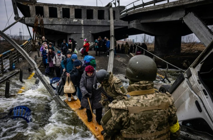 Des personnes évacuées traversent un pont détruit pour quitter la ville d'Irpin, au nord-ouest de Kiev, le 7 mars 2022.