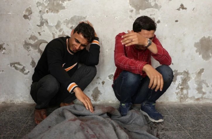 Des Palestiniens pleurent près d'un corps enveloppé dans une couverture à l'hôpital Al-Ahli, le 7 mai 2025, après une frappe israélienne dans la ville de Gaza