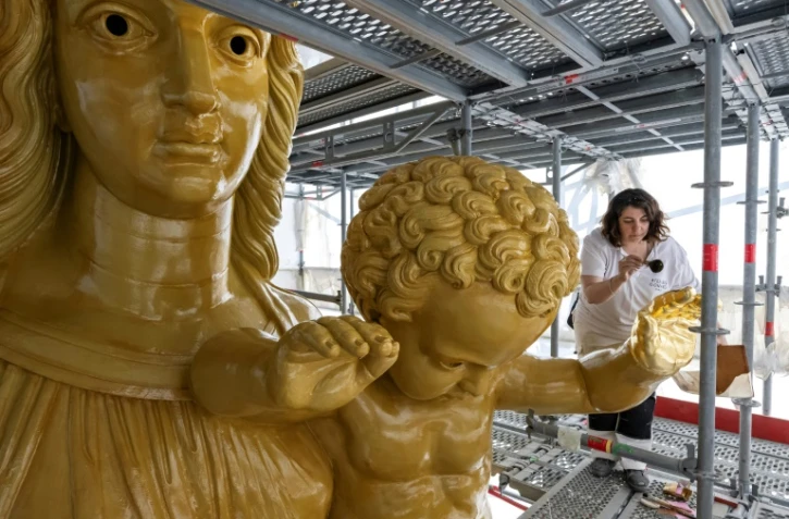 La restauratrice d'art Cyrielle D'Antoni travaille avec des feuilles d'or sur la statue de Jésus, à côté de la Vierge Marie, lors de la rénovation de la basilique Notre-Dame de la Garde à Marseille, le 3 septembre 2025