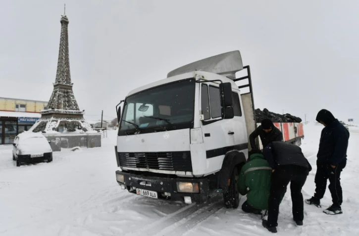 Des hommes changent le pneu d'un camion près d'une réplique de la tour Eiffel à Paris, nom officieux d'un village au Kirghizstan, le 22 janvier 2025