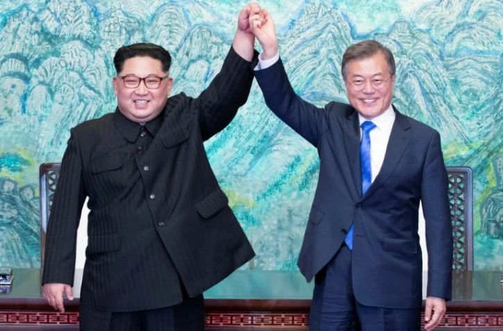 Le président sud-coréen Moon Jae-in (d) et le leader nord-coréen Kim Jong Un lèvent leurs mains unies pendant le sommet intercoréen, le 27 avril 2018 à Panmunjom