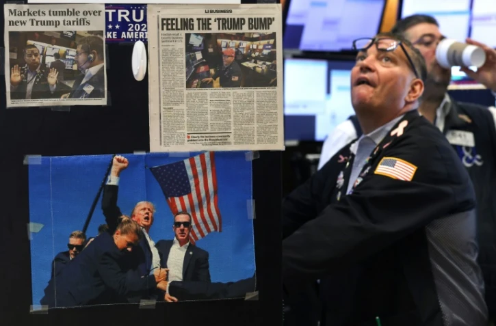 Des coupures de presse et une image du président américain Donald Trump affichées sur un bureau alors que les traders travaillent sur le parquet de la Bourse de New York (NYSE) à la cloche d'ouverture, le 9 avril 2025 à New York