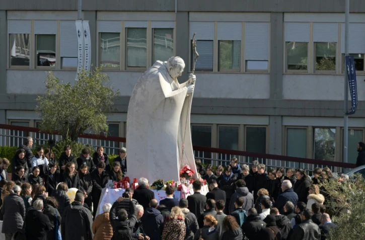 Des personnes prient autour de la statue de Jean-Paul II devant l'hôpital Gemelli à Rome où est hospitalisé le pape François, le 2 mars 2025