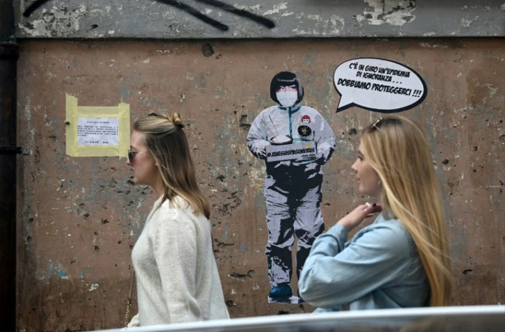 Deux femmes passent devant un message mural où il est écrit: "Il y a une épidémie d'ignorance dans l'air, nous devons nous protéger", par l'artiste Laika, près du quartier chinois de Rome, le 4 février 2020