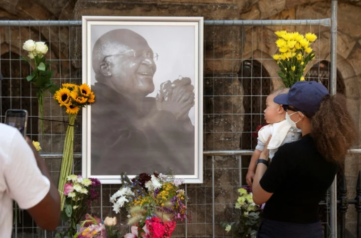 Des personnes déposent des fleurs auprès de l'effigie de Desmond Tutu accrochée devant la cathédrale Saint-Georges au Cap, le 26 décembre 2021