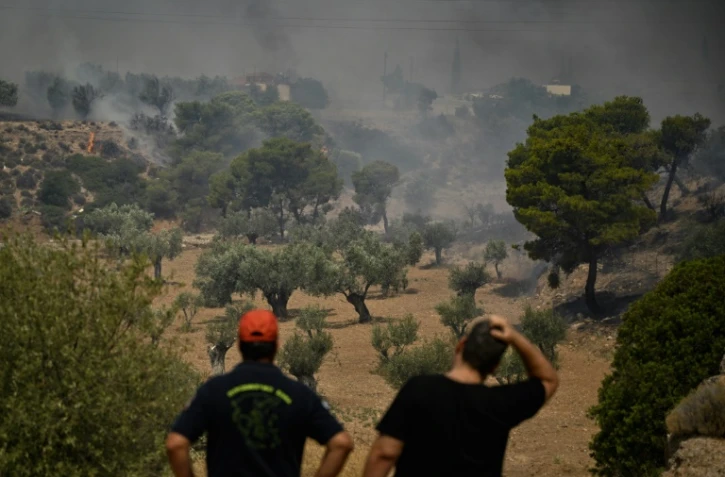 Un pompier (à gauche) et un habitant devant des feux de forêts près de Nea Peramos, à l'ouest d'Athènes, le 19 juillet 2023