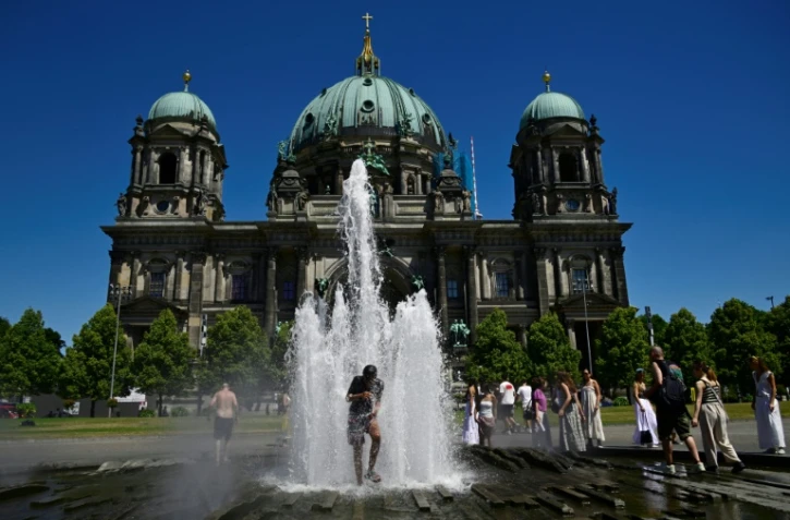 Des personnes se rafraîchissent dans l'eau d'une fontaine, le 2 juillet 2025 à Berlin
