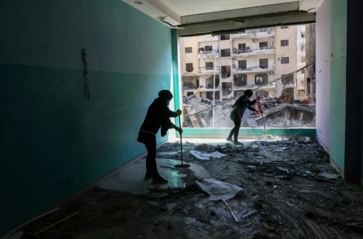 Des membres du personnel d'une ONG libanaise nettoient les débris dans leurs locaux endommagés par une frappe israélienne sur un bâtiment voisin, dans la banlieue sud de Beyrouth, le 2 décembre 2024