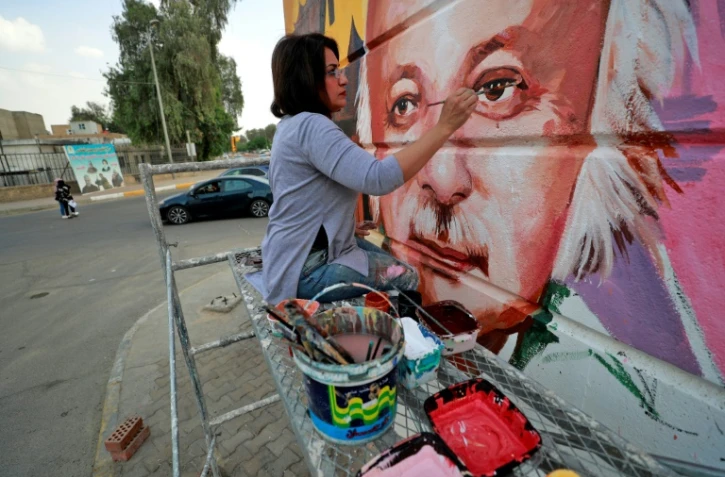 L'artisqte irakienne Wijdan al-Majed apporte quelques touches à une fresque du poète irakien Muzaffar al-Nawab sur un mur de Bagdad, le 26 avril 2022