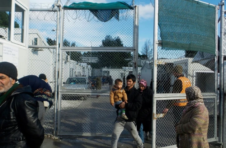 Des migrants avec un bébé sortent du camp migratoire de Moria, deuxième "ville" de l'île de Lesbos, le 21 décembre 2017 en Grèce