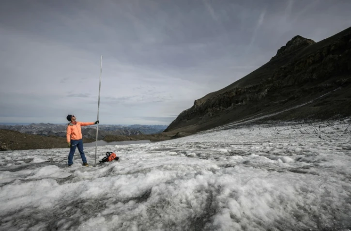 Le glaciologue Matthias Huss brandit une perche de mesure de quatre mètres de long, équivalant à la hauteur de la couche de glace ayant fondu en un an, le 24 septembre 2024 sur le glacier du Scex Rouge, en Suisse