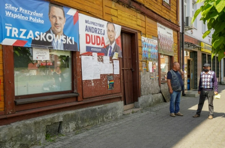 Deux hommes discutent devant des affiches de campagne des candidats du second tour de l'élection présidentielle polonaise le 9 juillet 2020 à Raciaz (Pologne)