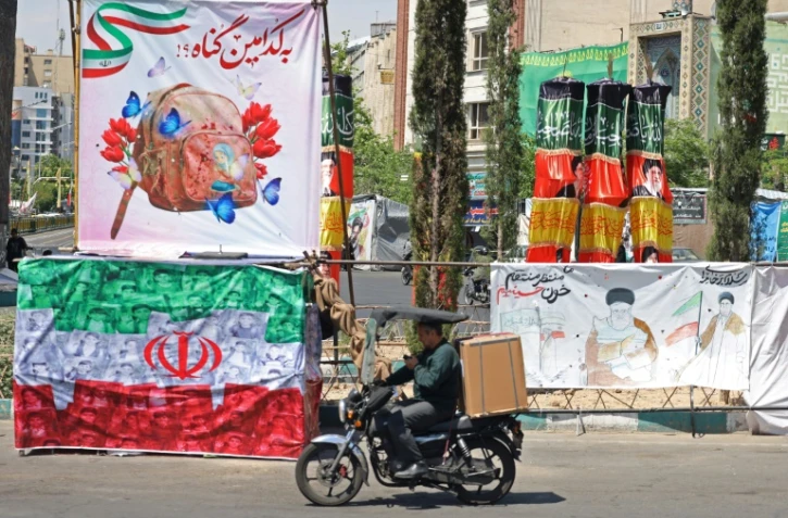 Un automobiliste passe devant une banderole représentant le guide suprême iranien tué, l'ayatollah Ali Khamenei, ainsi qu'un drapeau iranien, à Téhéran le 29 avril 2026
