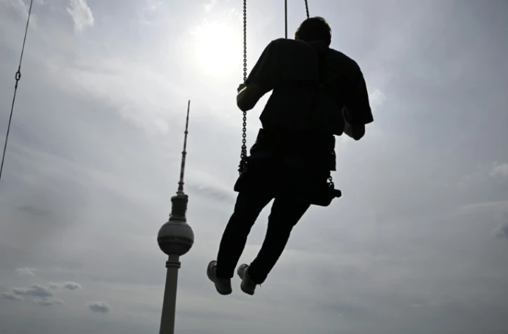 Un homme se balance à 120 mètres au dessus de Berlin sur la plus haute balançoire d'Europe, juchée sur le toit d'un hôtel face à la Fernsehturm, emblème touristique de la ville de l'Alexanderplatz, le 31 juillet 2024