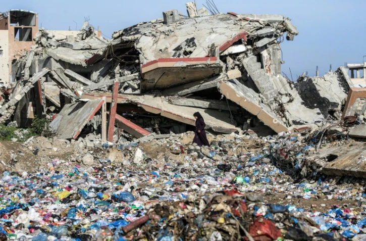 Une Palestinienne marche entre des détritus et un immeuble détruit, dans le camp de réfugiés de Nousseirat, dans le centre de la bande de Gaza, le 29 janvier 2026