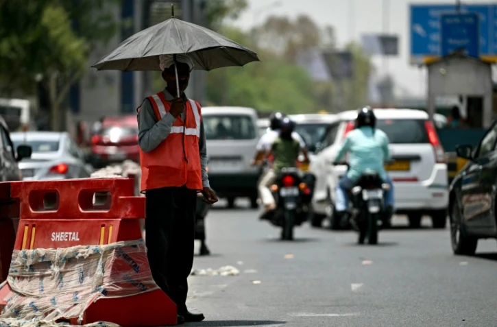 Un employé fait la ciculation protégé par un parapluie par les fortes chaleurs à New Delhi, en Inde, le 29 mai 2024