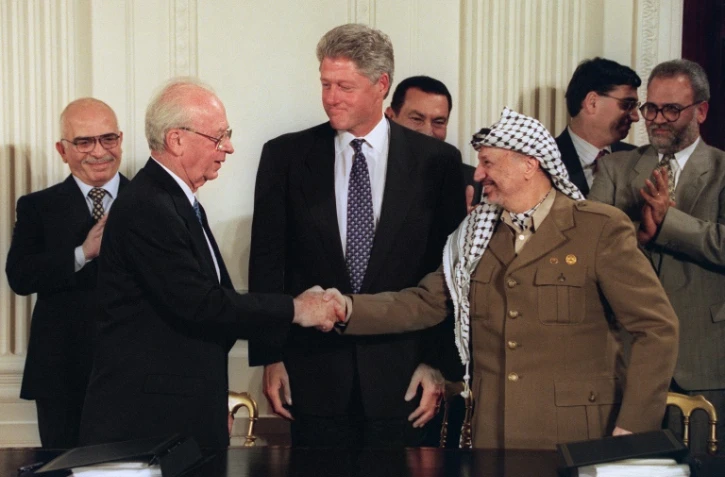 Le 28 septembre 1995, le président américain Bill Clinton (C) observe le premier ministre israélien Yitzhak Rabin (2e D) et Yasser Arafat (2e D), dirigeant de l'OLP, se serrer la main après la signature d'un accord, à Washington.