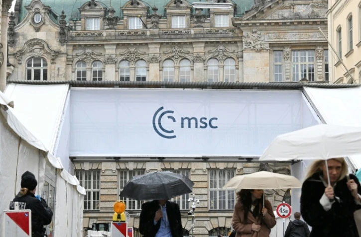 Des gens s'abritent de la pluie en passant devant un accès à la Conférence de Munich sur la sécurité (MSC), le 12 février 2026 à Munich