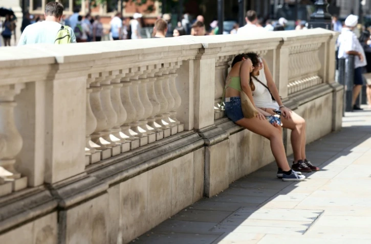 Des personnes se protégent du soleil derrière un mur, le 24 juin 2026 à Londres