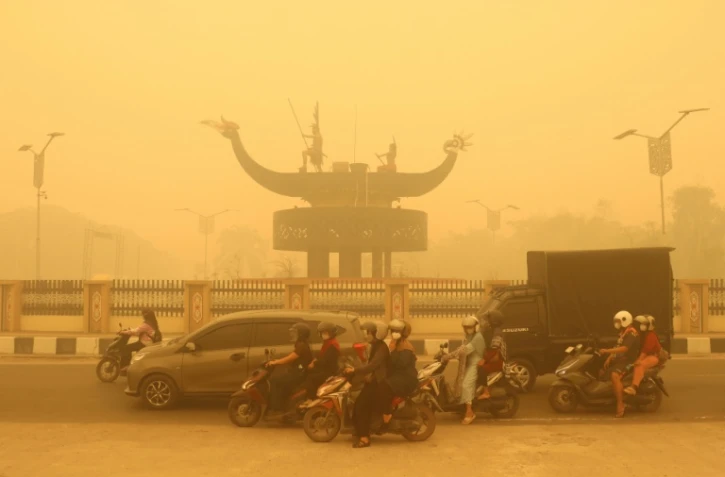 Des motocyclistes portant un masque de protection circulent dans une épaisse brume causée par des feux de forêt et de terres dans la région de Palangkaraya, dans le Kalimantan central, le 24 octobre 2026 en Indonésie