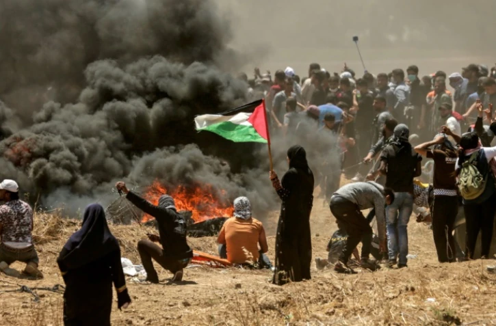 Une Palestinienne tient un drapeau durant les affrontements entre manifestants palestiniens et soldats israéliens à la frontière entre la bande de Gaza et Israël, le 14 mai 2018