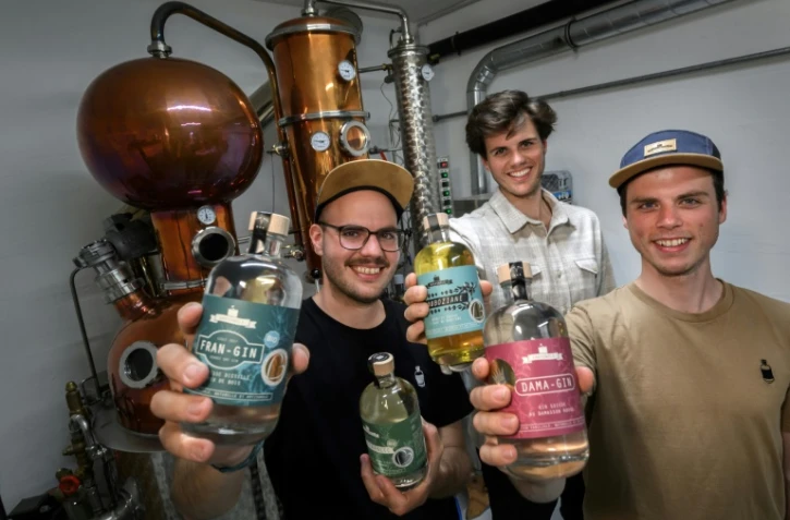 (g-d) Les frères Gyger, Gaetan, Luca et Tim, montrent des bouteilles de gin et de gentiane devant l'alambique de leur distillerie Gagygnole de Souboz, le 10 mai 2022 en Suisse
