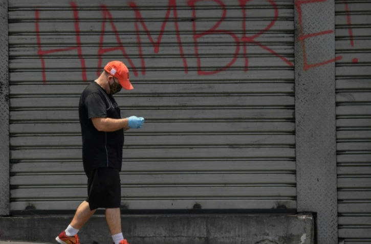 Un homme, protégé par un masque contre le coronavirus, passe devant un rideau de fer où est écrit "Faim", à Caracas, le 14 mai 2020