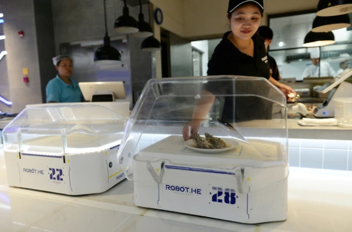 Une employée du restaurant Robot.He dépose un plat sur le robot serveur, le 30 juillet 2018 à Shanghai, en Chine