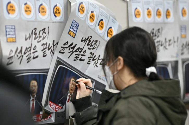 Une femme écrit sur une affiche représentant le président sud-coréen Yoon Suk Yeol "l'insurrection criminelle de Yoon est terminée" dans une station de métro à Séoul, le 9 décembre 2024