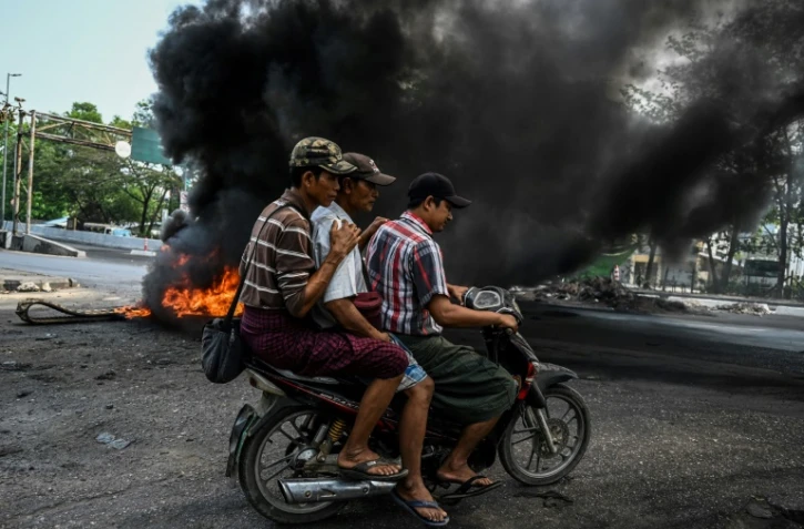 Des hommes à moto passent près d'une barricade en feu, à Rangoun en Birmanie le 17 mars 2021