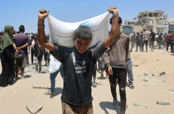 Des personnes se déplacent dans la rue al-Rashid, dans l'ouest de Jabalia, le 22 juillet 2025, après avoir reçu une aide humanitaire dans un centre de distribution situé dans le nord de la bande de Gaza