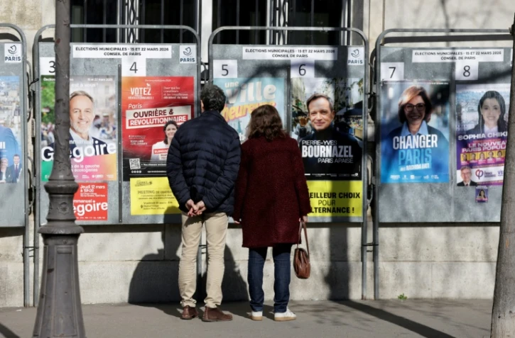 Des passants regardent les affiches électorales des candidats aux municipales à Paris le 9 mars 2026