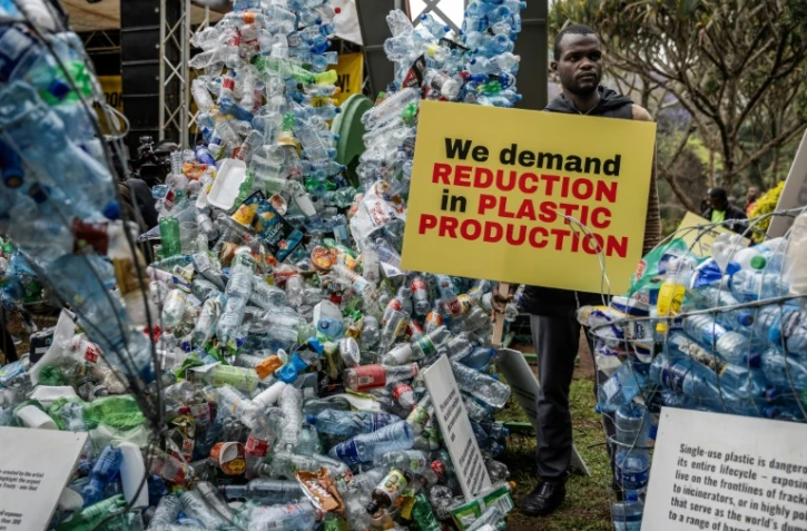 Un militant pour le climat tient une banderole à côté d'une installation de déchets en plastique, le 11 novembre 2023 à Nairobi, au Kenya, avant une réunion de 175 pays pour négocier des mesures concrètes pour lutter contre la pollution plastique