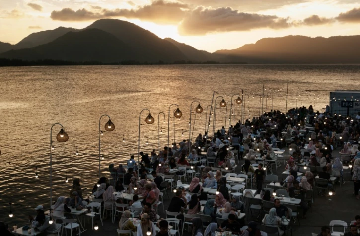 Des personnes attablées en bord de mer sur la terrasse d'un café construit sur le site où toutes les maisons ont été détruites par le tsunami de 2004 dans l'océan Indien, à Banda Aceh, le 25 décembre 2024, à la veille du 20e anniversaire de la catastrophe