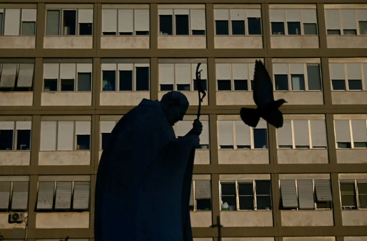 Un pigeon vole devant la statue du pape Jean-Paul II à l'extérieur de l'hôpital Gemelli où le pape François est hospitalisé pour une pneumonie, à Rome le 19 mars 2025