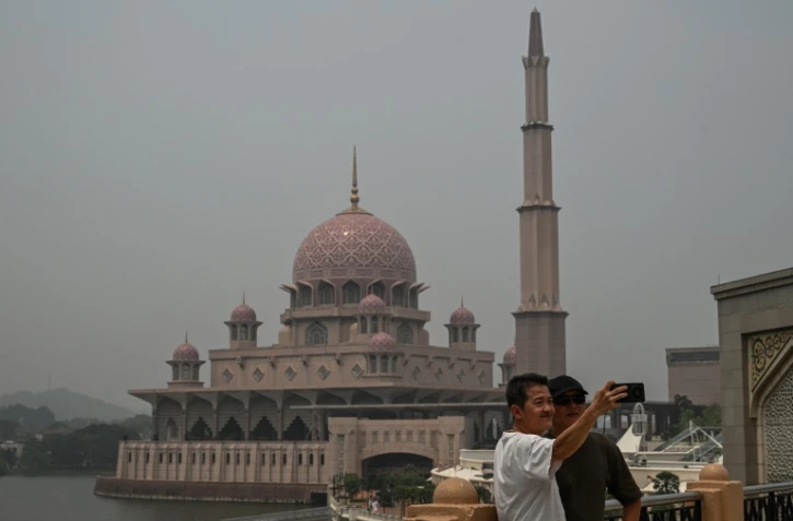Deux personnes se prennent en photo devant une mosquée dans un air saturé par des fumées toxiques, à Putrajaya, en Malaisie, le 17 octobre 2026